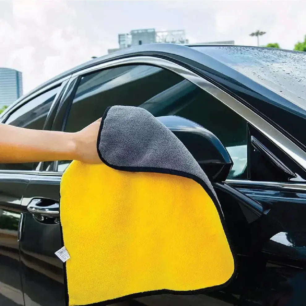 Person cleaning a car window with a yellow and gray microfiber cloth.