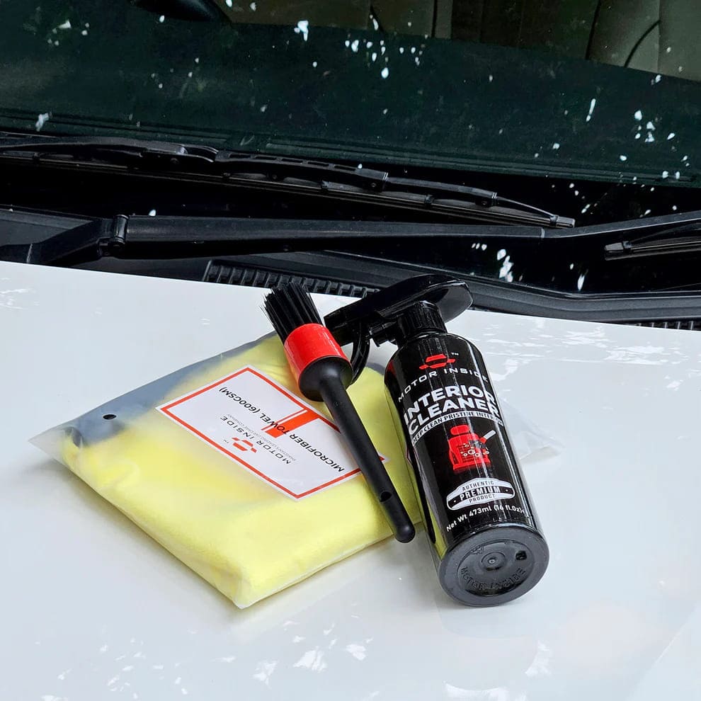 Interior cleaner with microfiber towel and detailing brush on a car bonnet